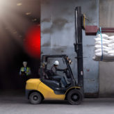Forklift handling sugar bags outside from warehouse for stuffing into container for export.